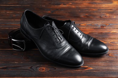 Photo of Pair of black leather shoes and belt on wooden table, closeup