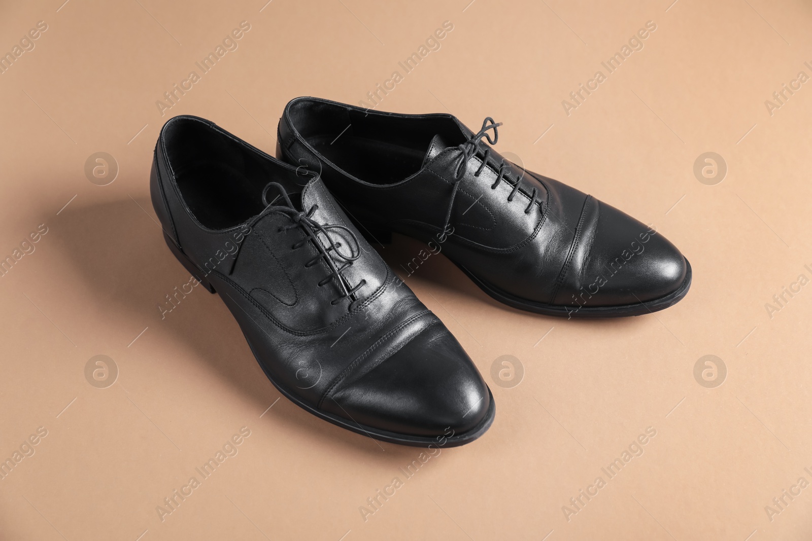 Photo of Pair of black leather shoes on beige background