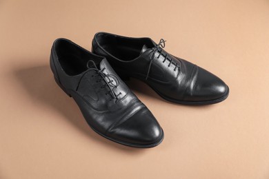 Photo of Pair of black leather shoes on beige background
