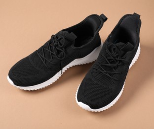 Photo of Pair of black sneakers on beige background