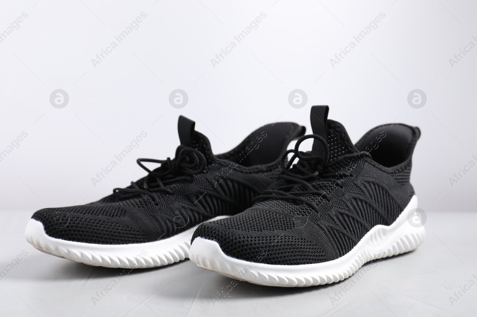 Photo of Pair of black sneakers on light grey surface, closeup