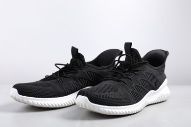 Photo of Pair of black sneakers on light grey surface, closeup