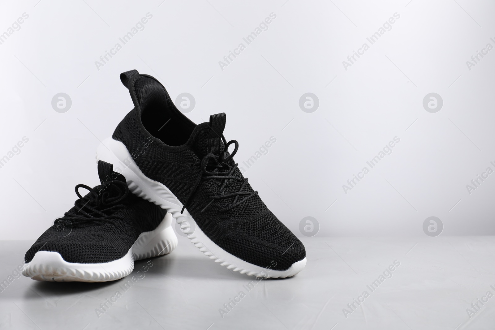 Photo of Pair of black sneakers on light grey surface, space for text