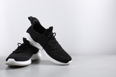 Photo of Pair of black sneakers on light grey surface, space for text