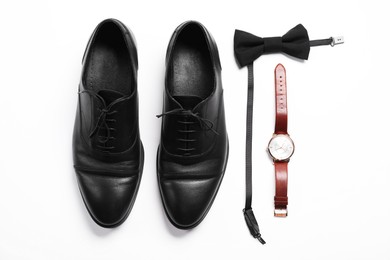 Photo of Pair of black leather shoes, bow tie and wrist watch on white background, flat lay