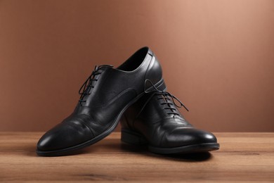 Photo of Pair of black leather shoes on wooden surface against brown background