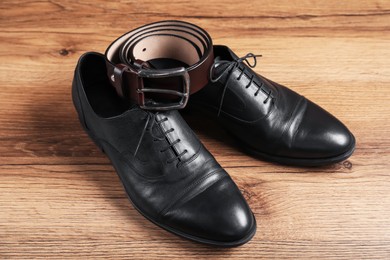 Photo of Pair of black leather shoes and belt on wooden surface, closeup
