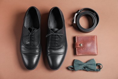 Photo of Pair of black leather shoes, belt, bow tie and purse on dark beige background, flat lay