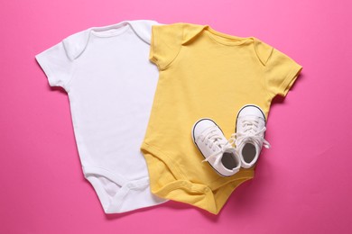 Photo of Bright baby onesies and shoes on pink background, flat lay