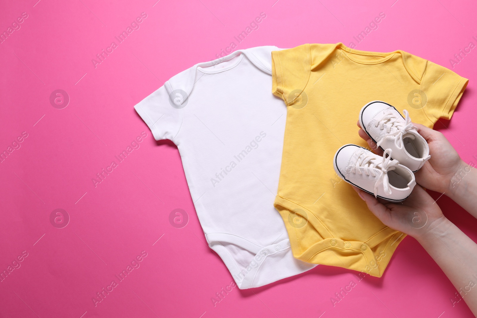 Photo of Woman with baby shoes and onesies on pink background, top view. Space for text