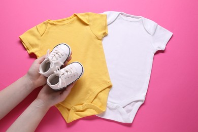 Photo of Woman with baby shoes and onesies on pink background, top view