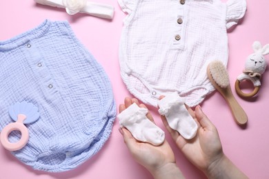 Photo of Woman with baby socks, clothes and accessories on pink background, top view