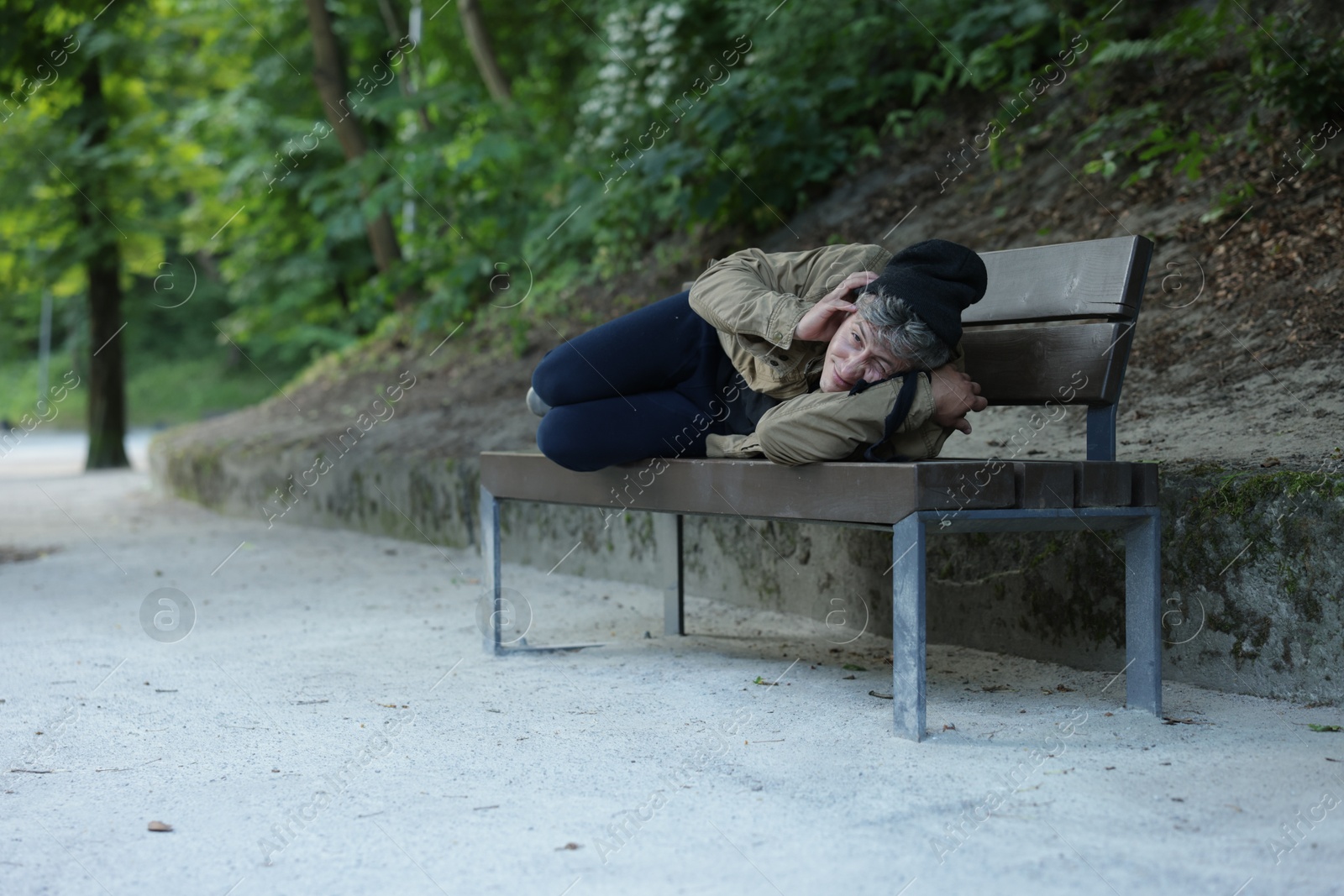 Photo of Homeless man lying on bench in park, space for text