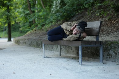 Photo of Homeless man lying on bench in park, space for text