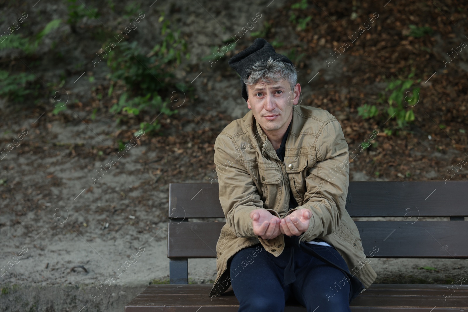 Photo of Homeless man begging for money on bench in park, space for text