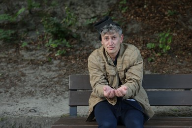 Photo of Homeless man begging for money on bench in park, space for text