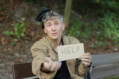 Photo of Homeless man with sign Help begging for money on bench in park