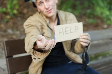 Photo of Homeless man with sign Help begging for money on bench in park, selective focus