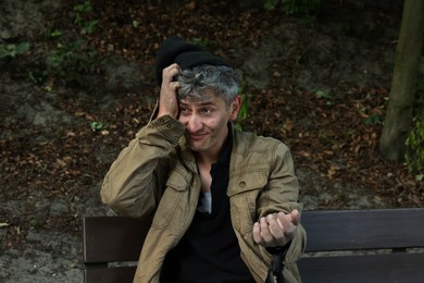 Photo of Homeless man begging for money on bench in park