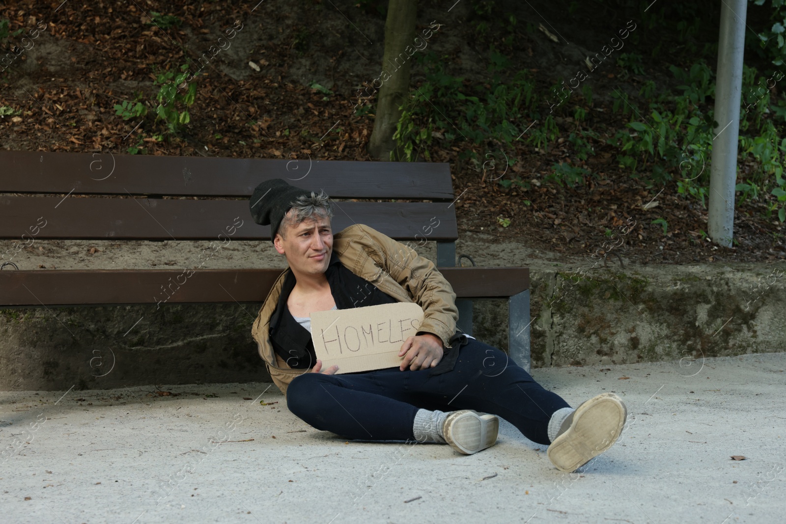 Photo of Poor man with sign Homeless near bench in park