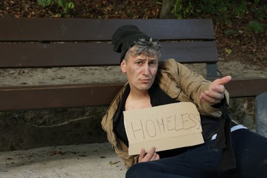Photo of Poor man with sign Homeless begging for money near bench in park