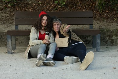 Photo of Homeless people begging for money near bench in park