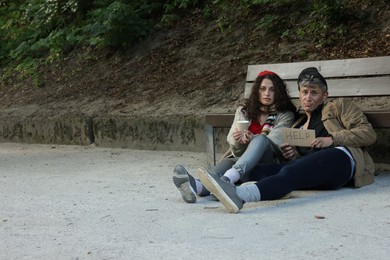 Photo of Homeless people with sign Help near bench in park, space for text