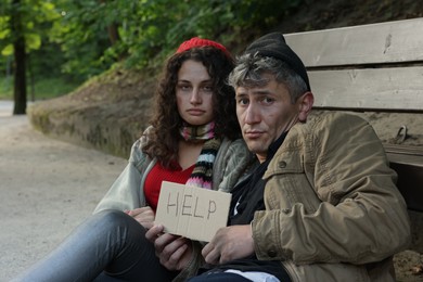 Photo of Homeless people with sign Help near bench in park