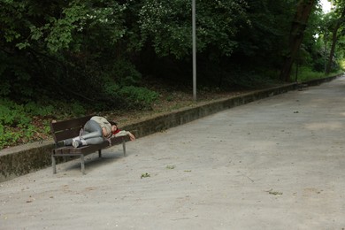 Photo of Homeless woman sleeping on bench in park, space for text