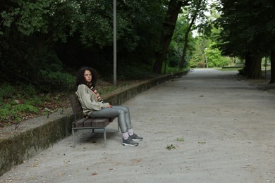 Photo of Homeless woman sitting on bench in park, space for text