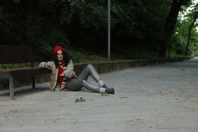 Photo of Homeless woman begging for money near bench in park, space for text