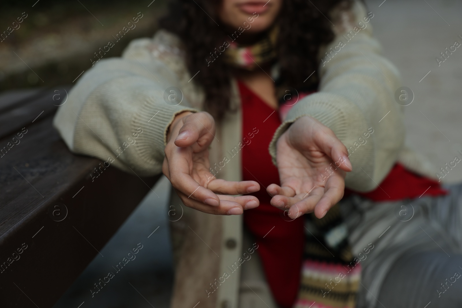 Photo of Homeless woman begging for money near bench in park, closeup