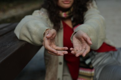 Photo of Homeless woman begging for money near bench in park, closeup