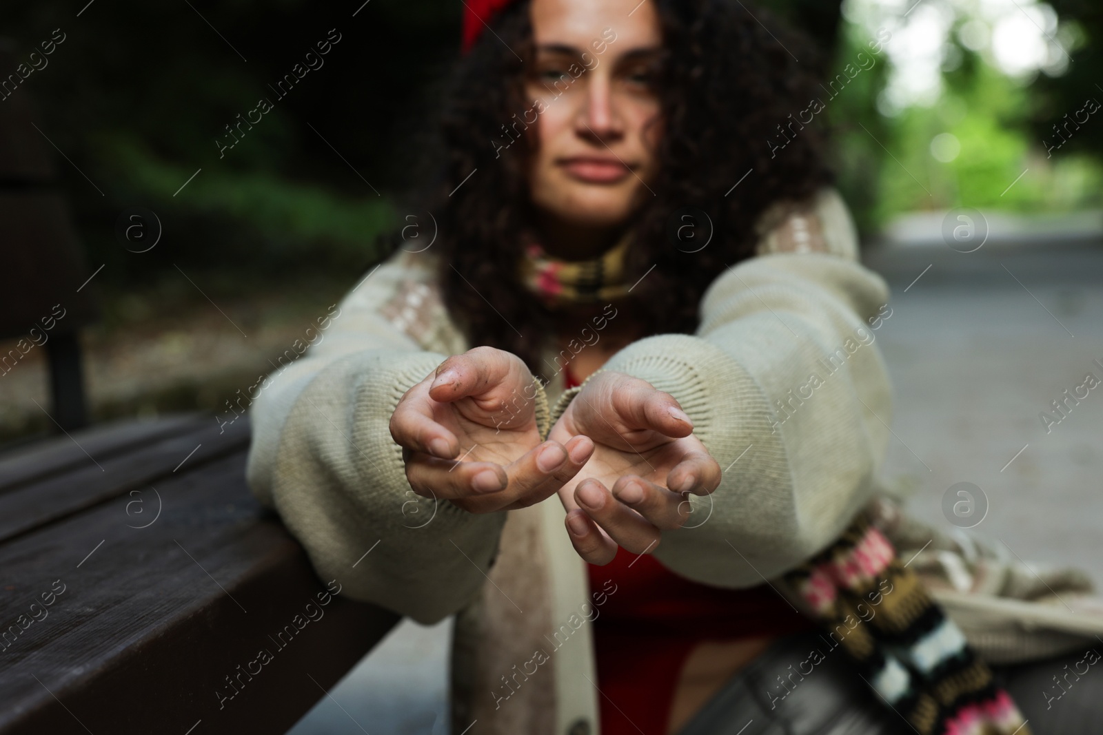 Homeless woman begging for money near bench in park, selective focus Photo of Homeless woman begging for money near bench in park, selective focus