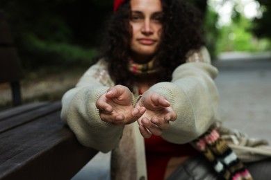 Photo of Homeless woman begging for money near bench in park, selective focus