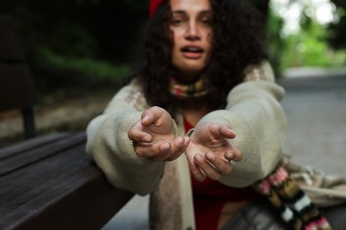 Photo of Homeless woman begging for money near bench in park, selective focus
