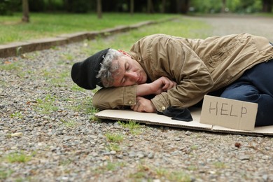 Photo of Homeless man with sign Help sleeping on carton in park