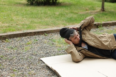 Photo of Homeless man lying on carton in park, space for text