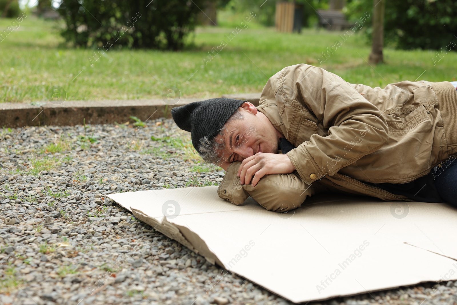 Photo of Homeless man lying on carton in park, space for text