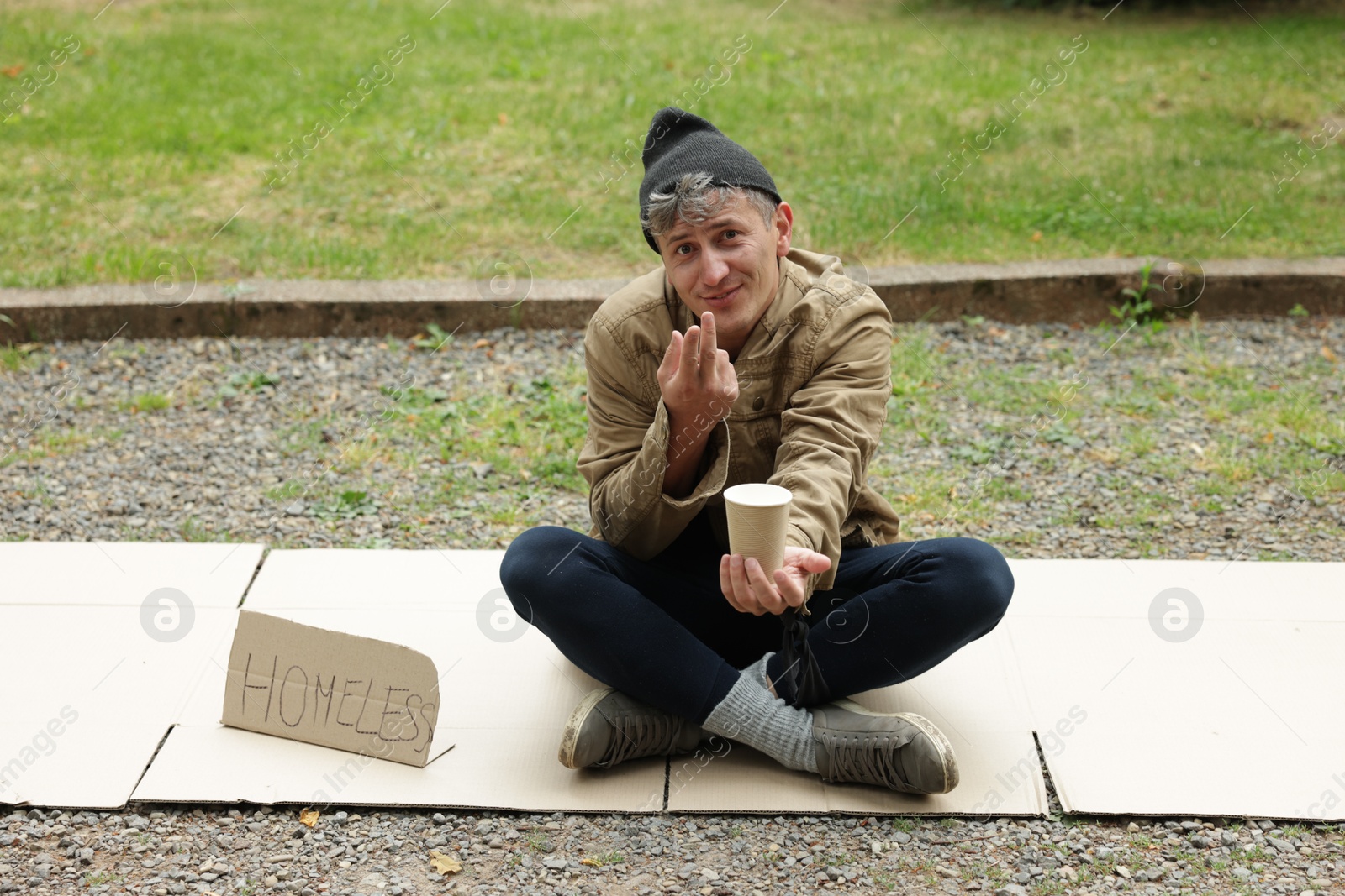 Photo of Poor man with sign Homeless and paper cup begging for money on carton in park