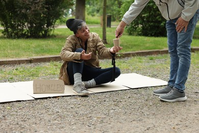 Photo of Man giving money to homeless person outdoors, closeup