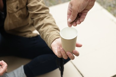 Photo of Man giving money to homeless person outdoors, closeup