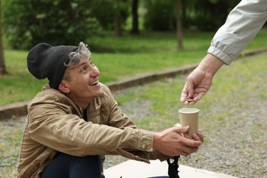 Photo of Man giving money to homeless person outdoors, closeup