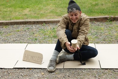 Photo of Poor man with sign Homeless and paper cup begging for money on carton in park