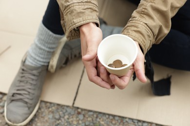Photo of Homeless man holding paper cup with coins on carton outdoors, above view