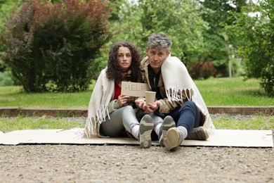 Photo of Homeless people with sign Help and paper cup on carton in park
