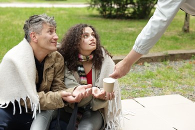 Photo of Man giving money to homeless people in park, closeup