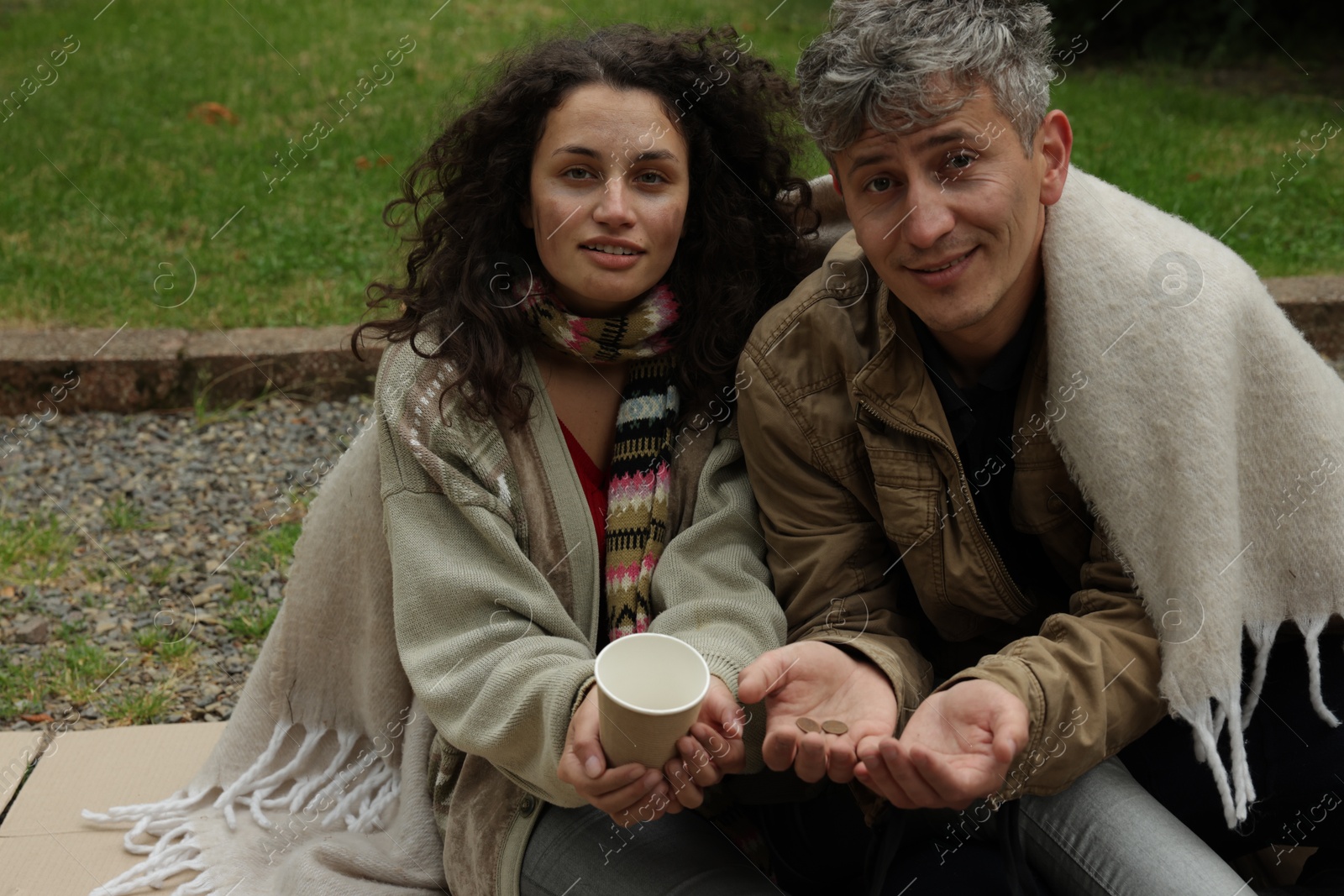 Photo of Homeless people with paper cup begging for money on carton outdoors
