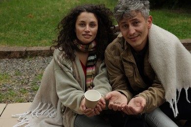 Photo of Homeless people with paper cup begging for money on carton outdoors