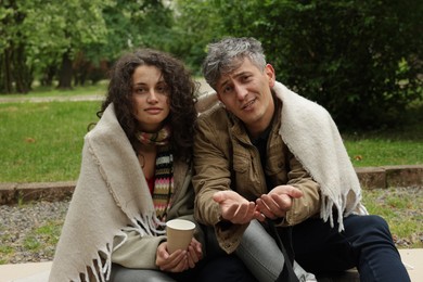 Photo of Homeless people with paper cup begging for money on carton outdoors